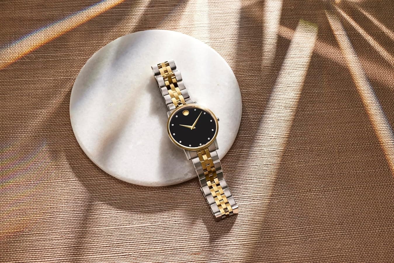 Two-tone Movado Museum Classic with a black dial, resting on a marble coaster